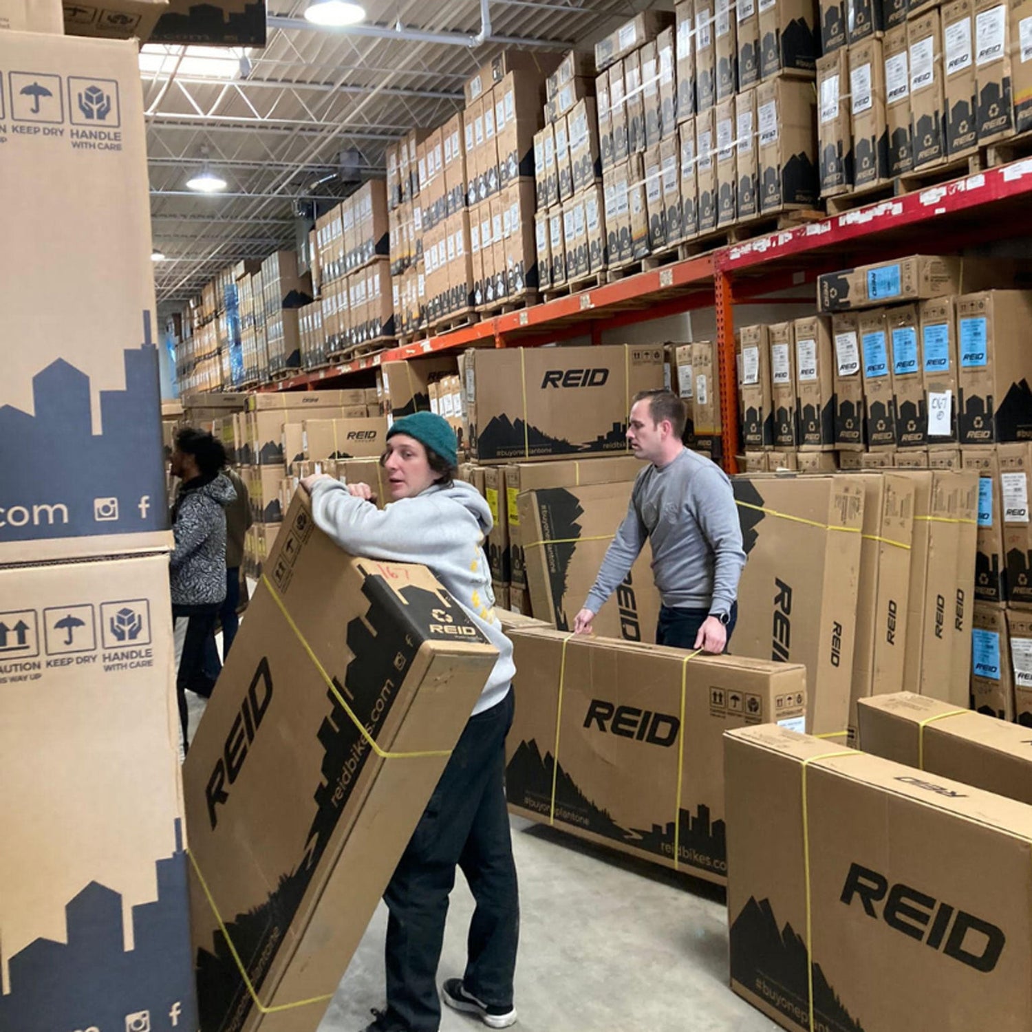 People moving Reid branded bike boxes in a busy warehouse 